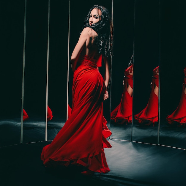 Portrait de belle femme brune en chaussures rouges et robe debout près des miroirs