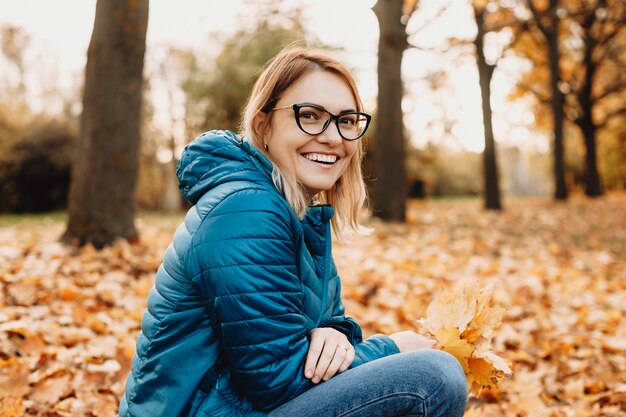 Portrait d'une belle femme caucasienne regardant la caméra en riant tout en portant des lunettes à l'extérieur dans le parc.