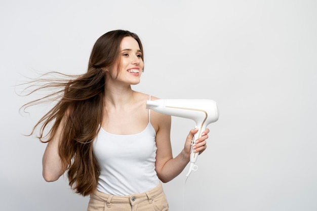 Portrait d'une belle femme caucasienne souriante utilisant un sèche-cheveux isolé sur un fond blanc