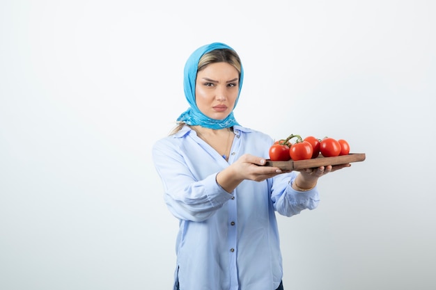 Portrait de belle femme en châle bleu tenant une planche de bois de tomates rouges