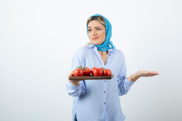 Portrait de belle femme en châle bleu tenant une planche de bois de tomates rouges