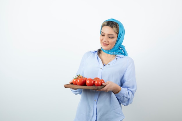 Portrait de belle femme en châle bleu tenant une planche de bois de tomates rouges