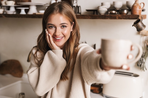 portrait de belle femme drôle portant des vêtements décontractés buvant du café dans une cuisine confortable