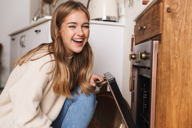 portrait d'une belle femme drôle portant des vêtements décontractés utilisant un four tout en préparant le dîner dans une cuisine confortable