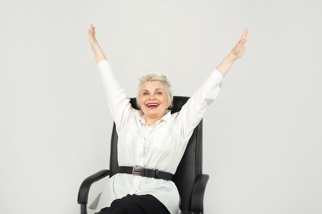 Portrait d'une belle femme élégante âgée dans des verres avec les mains levées assis sur une chaise