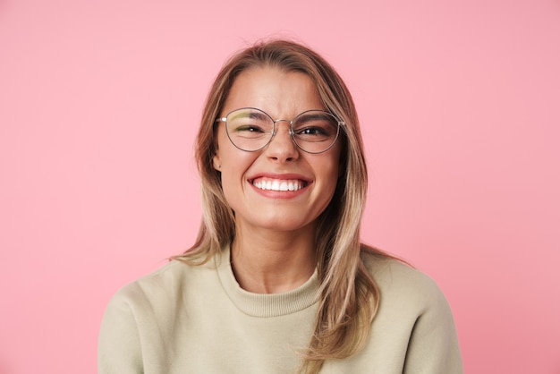 Portrait de belle femme excitée à lunettes souriant isolé sur rose