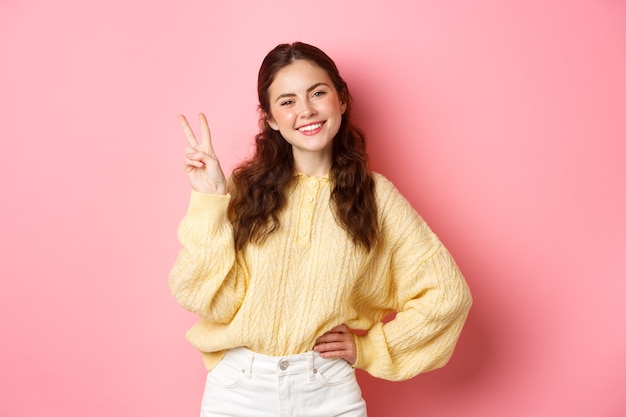 Portrait d'une belle femme heureuse montrant vsign et souriante tête inclinée mignonne faisant un geste de paix stan...