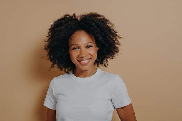 Portrait d'une belle femme joyeuse à la peau sombre se sentant heureuse isolée sur fond beige