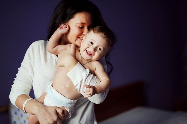 Portrait de belle femme joyeuse avec son bébé mignon s&#39;amuser ensemble à la maison. Doux garçon nu et mère brune.