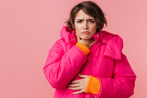 Portrait d'une belle femme malade en manteau chaud touchant sa gorge isolée sur rose