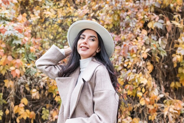 portrait d'une belle femme en manteau et chapeau sur fond de feuillage d'automne