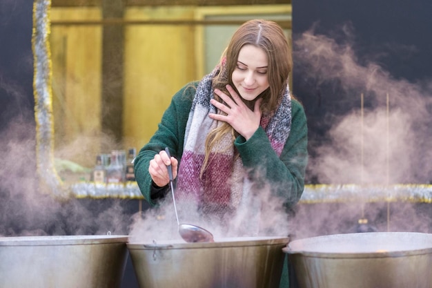 portrait d'une belle femme en manteau d'hiver dans des pots fumants avec une louche à la main