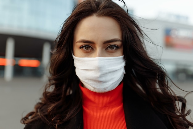 Portrait de belle femme marchant dans la rue portant un masque de protection comme protection contre les maladies infectieuses. Modèle malheureux attrayant avec la grippe à l'extérieur.