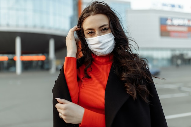 Portrait de belle femme marchant dans la rue portant un masque de protection comme protection contre les maladies infectieuses. Modèle malheureux attrayant avec la grippe à l'extérieur.