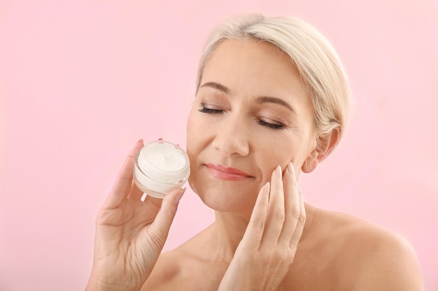 Portrait de belle femme mature avec pot de crème sur fond de couleur Concept de soins de la peau