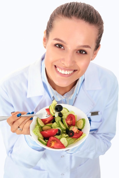 Portrait d'une belle femme médecin tenant une assiette avec des légumes frais