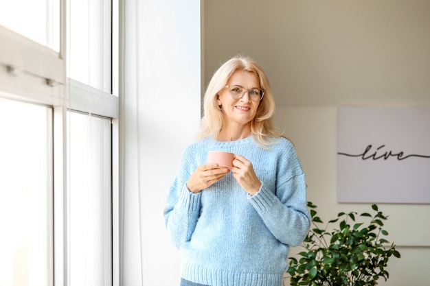 Portrait de belle femme mûre buvant du café près de la fenêtre