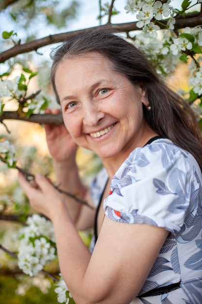 Portrait d'une belle femme mûre en robe légère sur fond de jardins fleuris au printemps