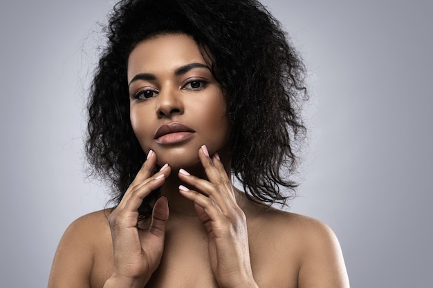 Portrait d'une belle femme noire à la peau lisse qui pose en studio sur fond gris