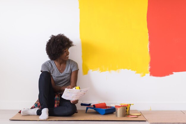 Portrait d'une belle femme peintre afro-américaine assise sur le sol près du mur après avoir peint.