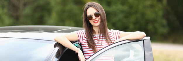 Portrait d'une belle femme portant des lunettes noires élégantes et posant près d'une voiture chic brune