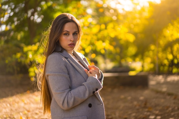 Portrait d'une belle femme profitant de l'automne dans un parc au coucher du soleil avec des arbres en arrière-plan