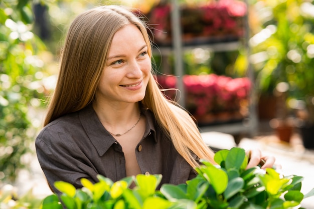 Portrait d'une belle femme qui travaille dans une serre avec des feuilles de plantes