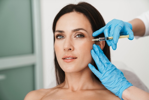 Portrait d'une belle femme recevant un traitement de mésothérapie au visage par un spécialiste des gants dans un salon de beauté