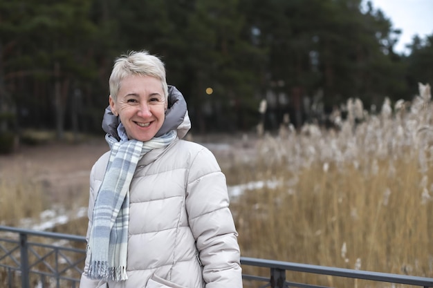 Portrait d'une belle femme retraitée senior âgée heureuse en âge à l'extérieur dans la forêt ou le parc en hiver