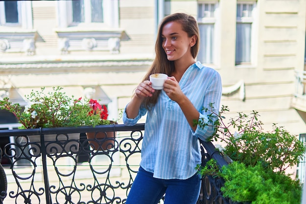 Portrait d'une belle femme romantique heureuse mignonne joyeuse souriante avec une tasse de café aromatique dans les mains le matin sur un balcon