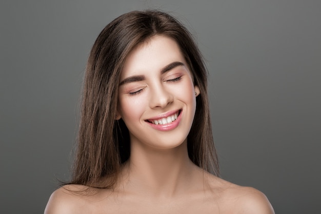 Portrait d'une belle femme souriante avec une peau parfaite et un maquillage naturel sur fond gris