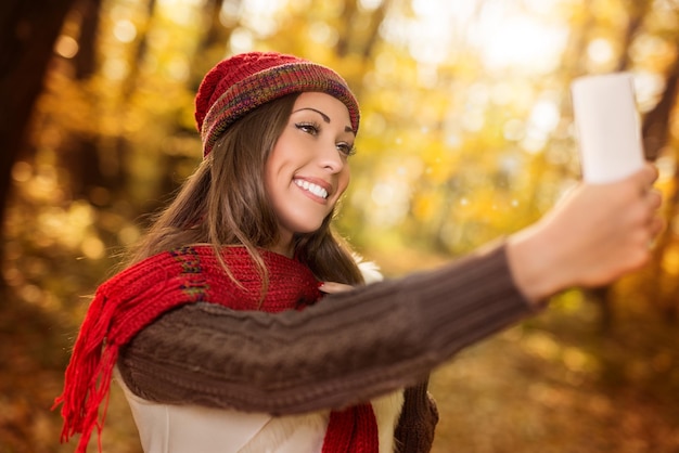 Portrait d'une belle femme souriante prenant selfie en forêt en automne.