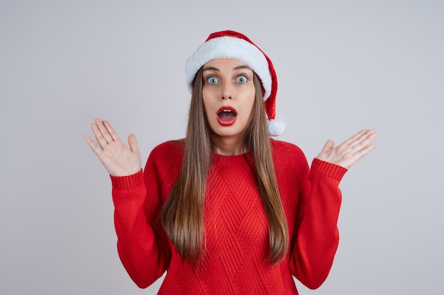 Portrait d'une belle femme surprise et émotionnelle dans un bonnet de Noel, pull rouge, tape dans ses mains. concept de vacances Noël