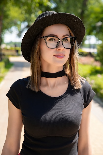 Portrait de la belle femme en t-shirt noir et jupe rouge marche et lunettes dans le parc