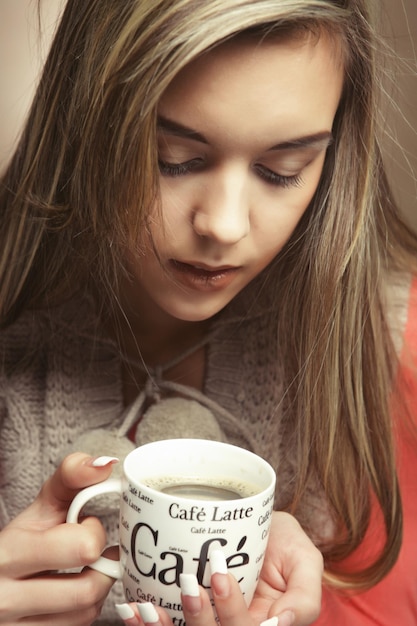 Portrait d'une belle femme avec une tasse de café debout sur le fond beige gros plan