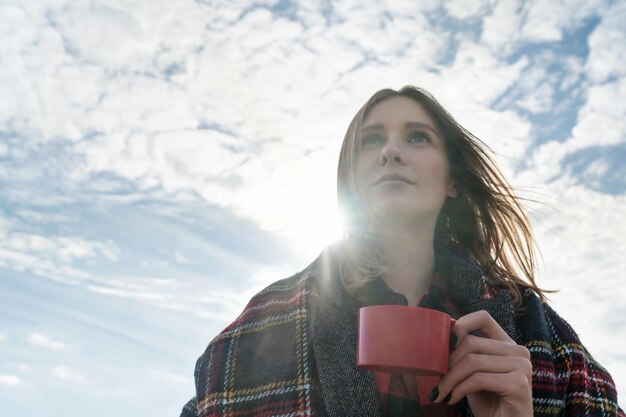 Portrait d'une belle femme avec une tasse à la main sur un fond de ciel nuageux