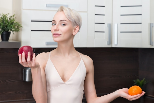 Portrait de belle femme tenant pomme et orange dans la cuisine moderne