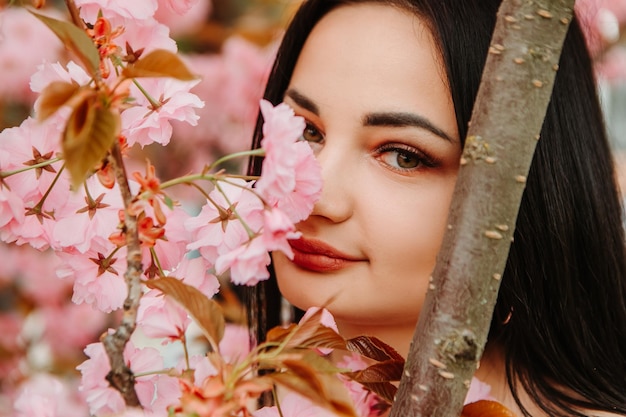 Portrait d'une belle femme tendre vêtue d'une robe fleurie rose posant près de fleurs de cerisier sakura