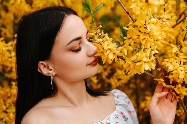 Portrait d'une belle femme tendre vêtue d'une robe fleurie rose posant près d'un forsythia jaune