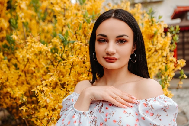 Portrait d'une belle femme tendre vêtue d'une robe fleurie rose posant près d'un forsythia jaune