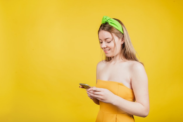 Portrait De Belle Femme Tenir Téléphone Look écran Sourire à Pleines Dents Isolé Sur Mur De Couleur Jaune. Envoi De Sms Dans Un Téléphone Intelligent