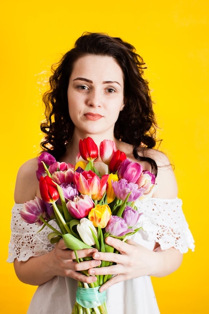 Le portrait d'une belle femme avec des tulipes isolées sur fond jaune