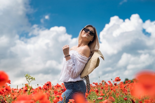 Portrait de la belle femme ukrainienne aux cheveux blonds, portant un chemisier blanc, posant dans un champ de pavot à la journée ensoleillée