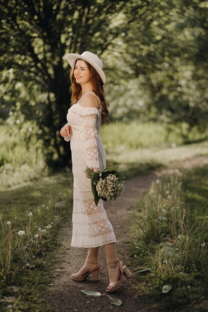 Portrait d'une belle femme vêtue d'une robe blanche et d'un chapeau avec des muguet une fille dans la nature