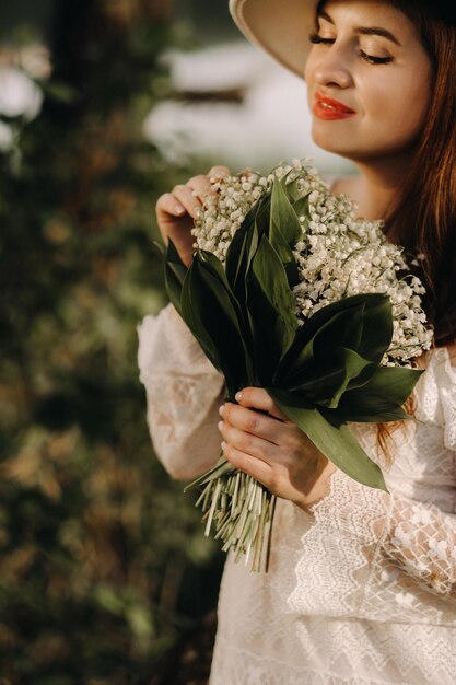 Portrait d'une belle femme vêtue d'une robe blanche et d'un chapeau avec des muguet une fille dans la nature