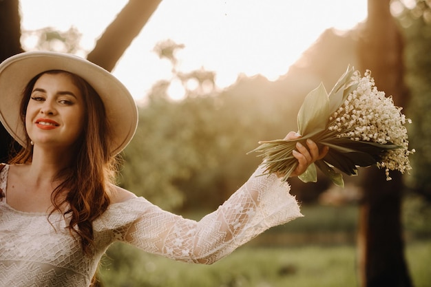 Portrait d'une belle femme vêtue d'une robe blanche et d'un chapeau avec des muguet une fille dans la nature