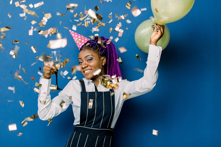 Photo portrait de la belle fille africaine en chapeau de fête rose tenant des ballons à air chaud et du champagne, au repos à la fête. africaine, femme, amusant, fête, confetti, bleu, espace