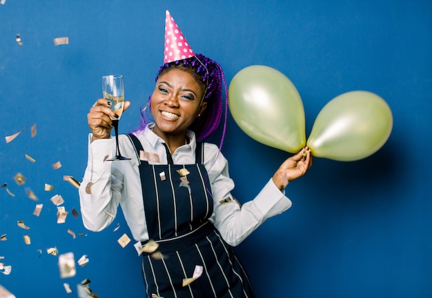 Portrait De La Belle Fille Africaine En Chapeau De Fête Rose Tenant Des Ballons à Air Chaud Et Du Champagne, Au Repos à La Fête. Africaine, Femme, Amusant, Fête, Confetti, Bleu, Espace