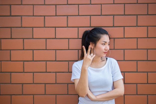 Portrait d'une belle fille asiatique chic pose pour prendre une photo sur un mur de briques