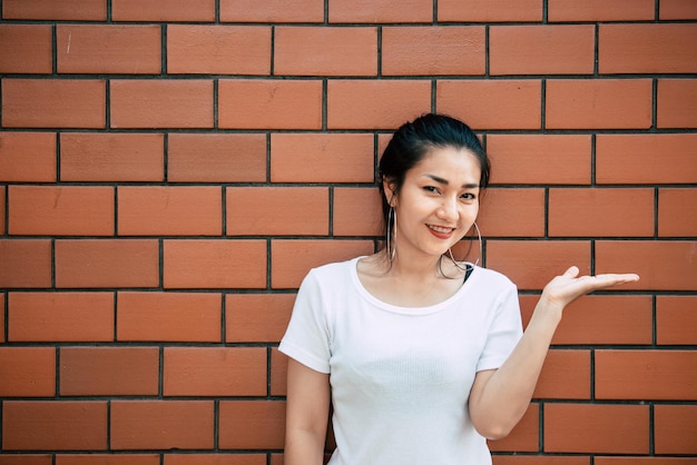 Portrait d'une belle fille asiatique chic pose pour prendre une photo sur un mur de briques